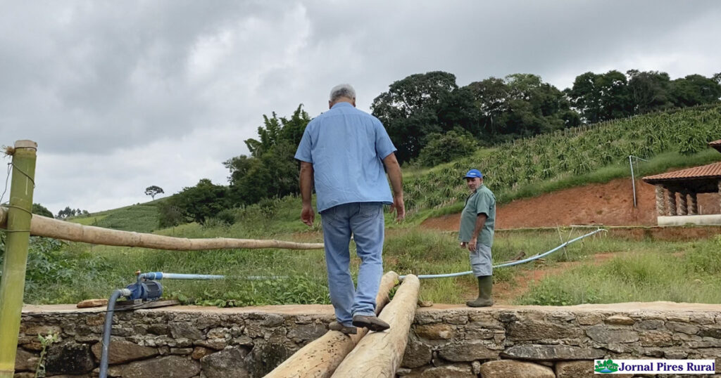 O agrônomo Hiromitsu Gervásio Ishikawa atravessando a ponte improvisada, observado pelo produtor José Franco de Moraes tendo afundo, atrás da casa, o pomar de pitayas